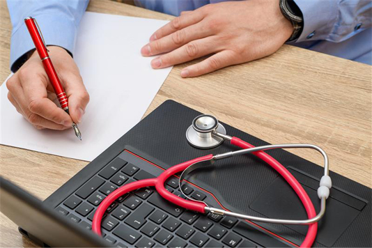 Person about to start writing on a sheet of paper; next to an open laptop with stethoscope laying on top.
