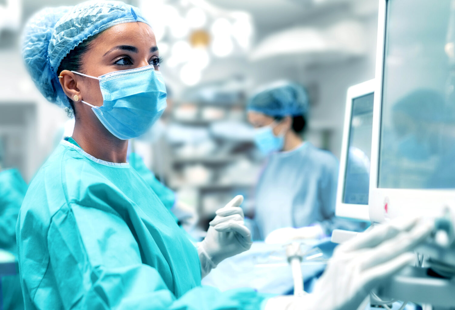 Veterinarian or technician in surgical scrubs reviewing patient vitals on a monitor.