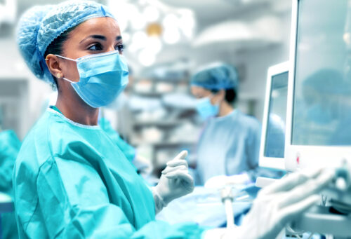 Veterinarian or technician in surgical scrubs reviewing patient vitals on a monitor.