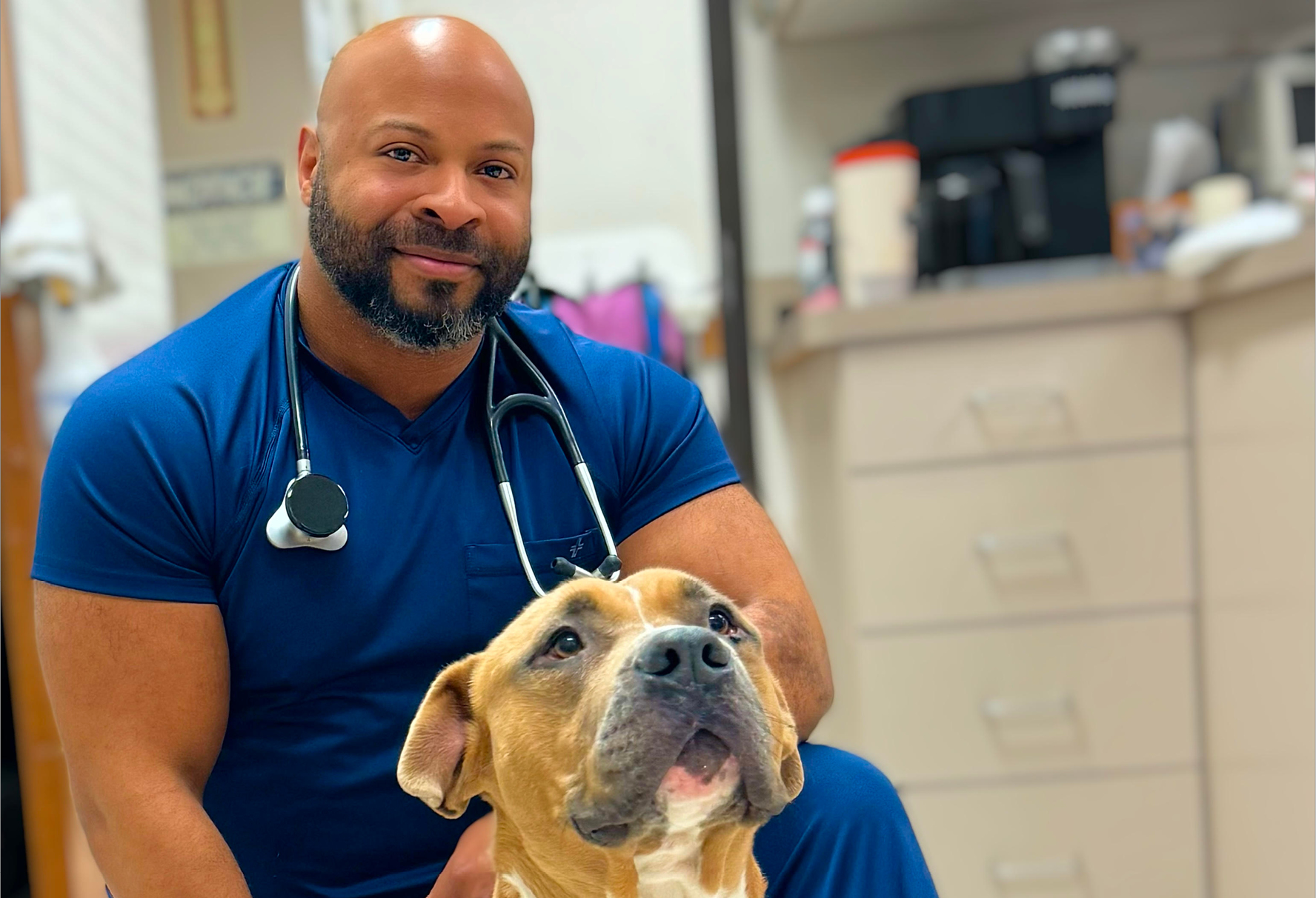 Photo of Anthony Hall, DVM, MPH, wearing athletic-style scrubs with a dog next to him