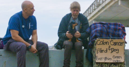 Photo of Kwane Stewart, DVM, talking to a homeless man holding a small dog. A sign is next to the homeless man that reads, 