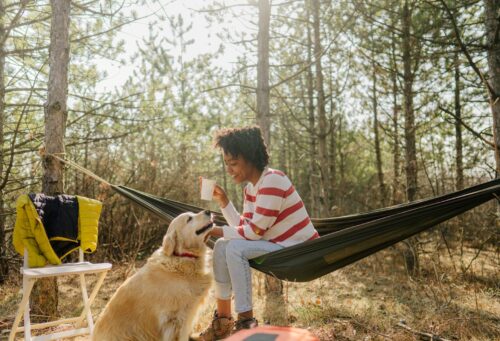 Black woman in hammock outdoors with dog and coffee