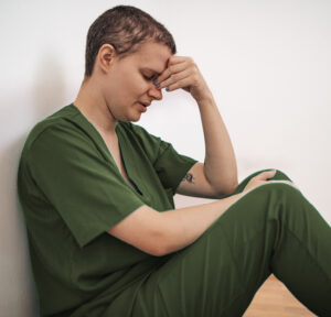 person in scrubs with head in hands